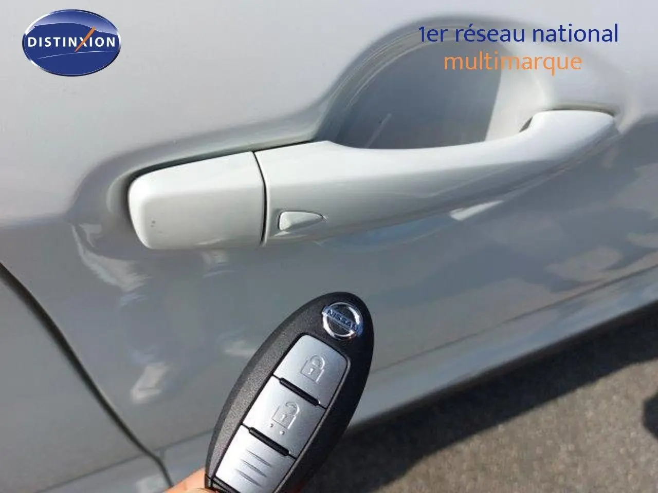 Gros plan sur la poignée de porte côté gauche d'un Nissan Qashqai blanc lunaire avec une clé mains libres visible.