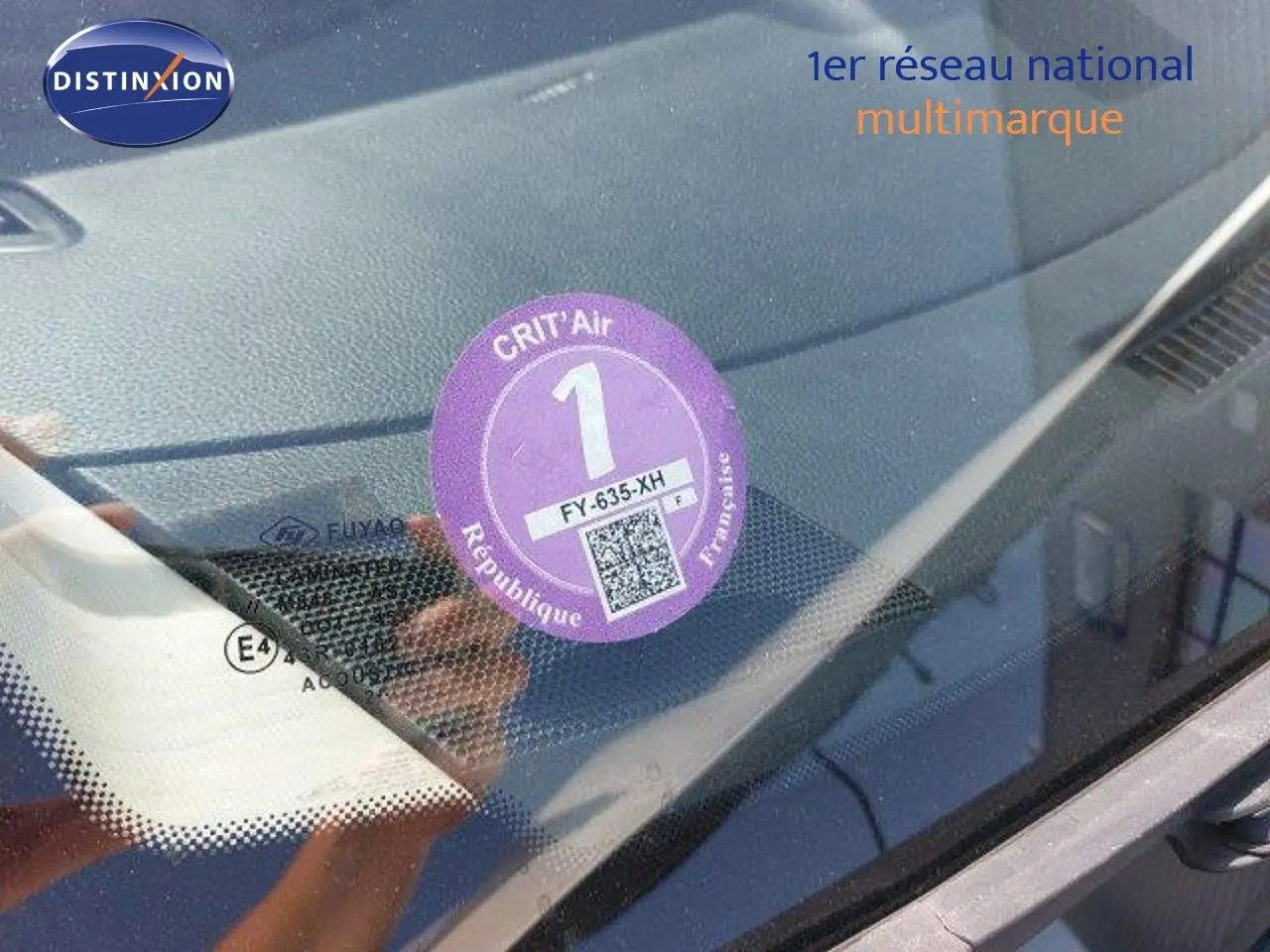 Vue rapprochée du pare-brise d'un Nissan Qashqai blanc lunaire avec vignette Crit'Air 1 apposée côté gauche.