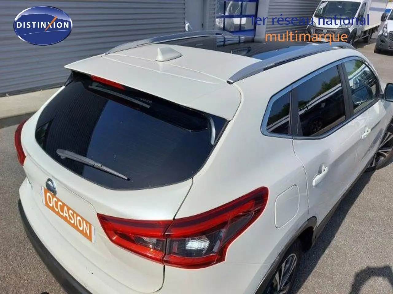 Vue 3/4 arrière droite d'un Nissan Qashqai blanc lunaire métallisé avec vitres teintées et toit équipé d'une antenne requin.