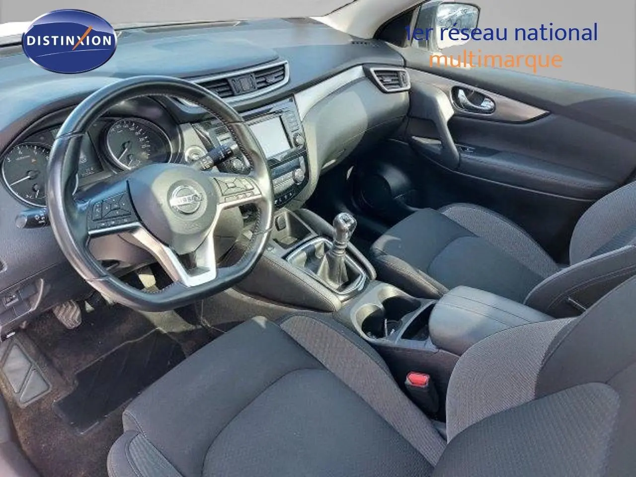 Intérieur du Nissan Qashqai 2019 vu côté conducteur, tableau de bord noir avec boîte manuelle et sièges tissu gris.