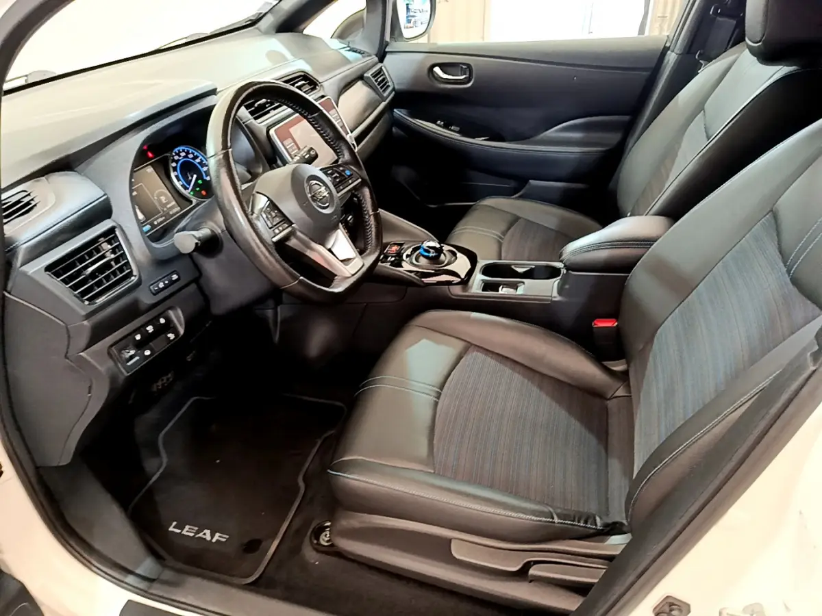 Vue intérieure côté conducteur du Nissan Leaf blanc 2020, montrant sièges cuir et tableau de bord avec écran tactile.