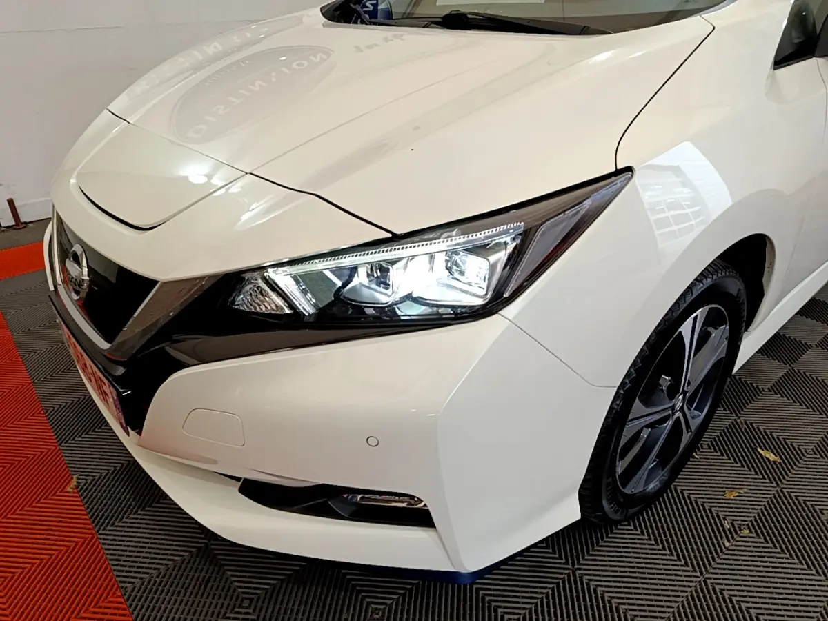 Vue 3/4 avant droit d'une Nissan Leaf blanche avec phares LED allumés et jantes alliage distinctives.