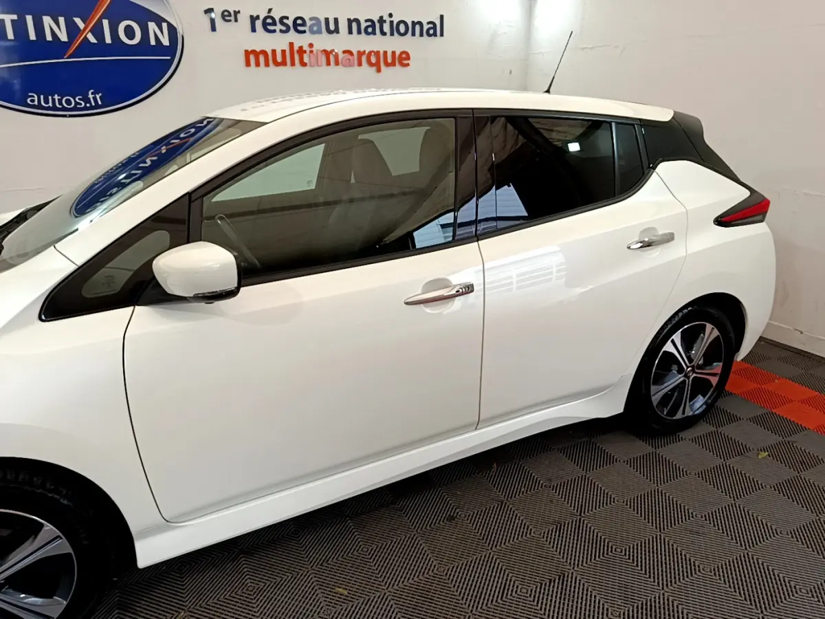 Profil côté gauche d'une Nissan Leaf blanche 2020 électrique, avec toit noir et jantes alliage distinctives.
