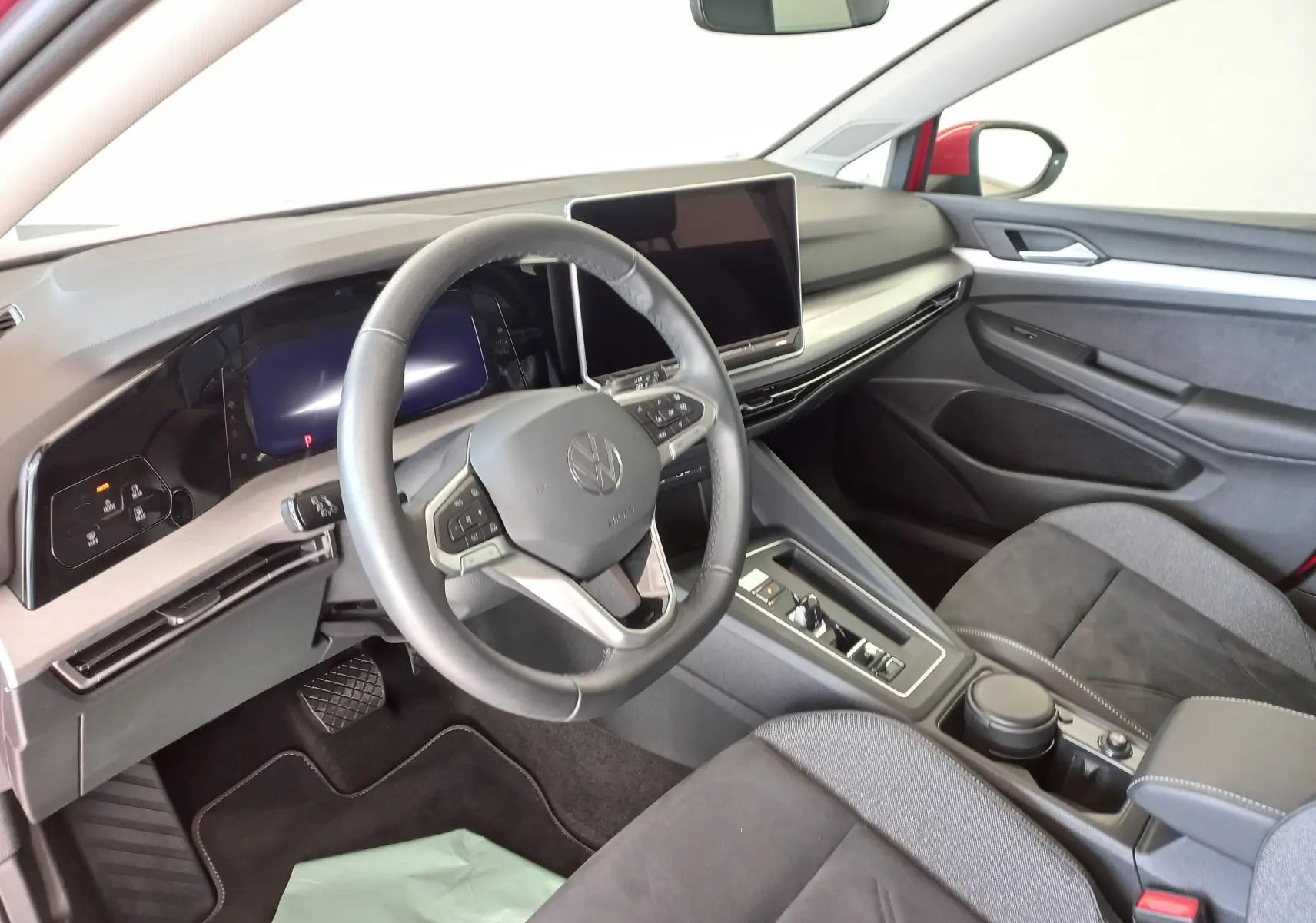 Vue intérieure côté conducteur de la Volkswagen Golf 2.0 TDI rouge, avec volant cuir multifonction et écran tactile central.