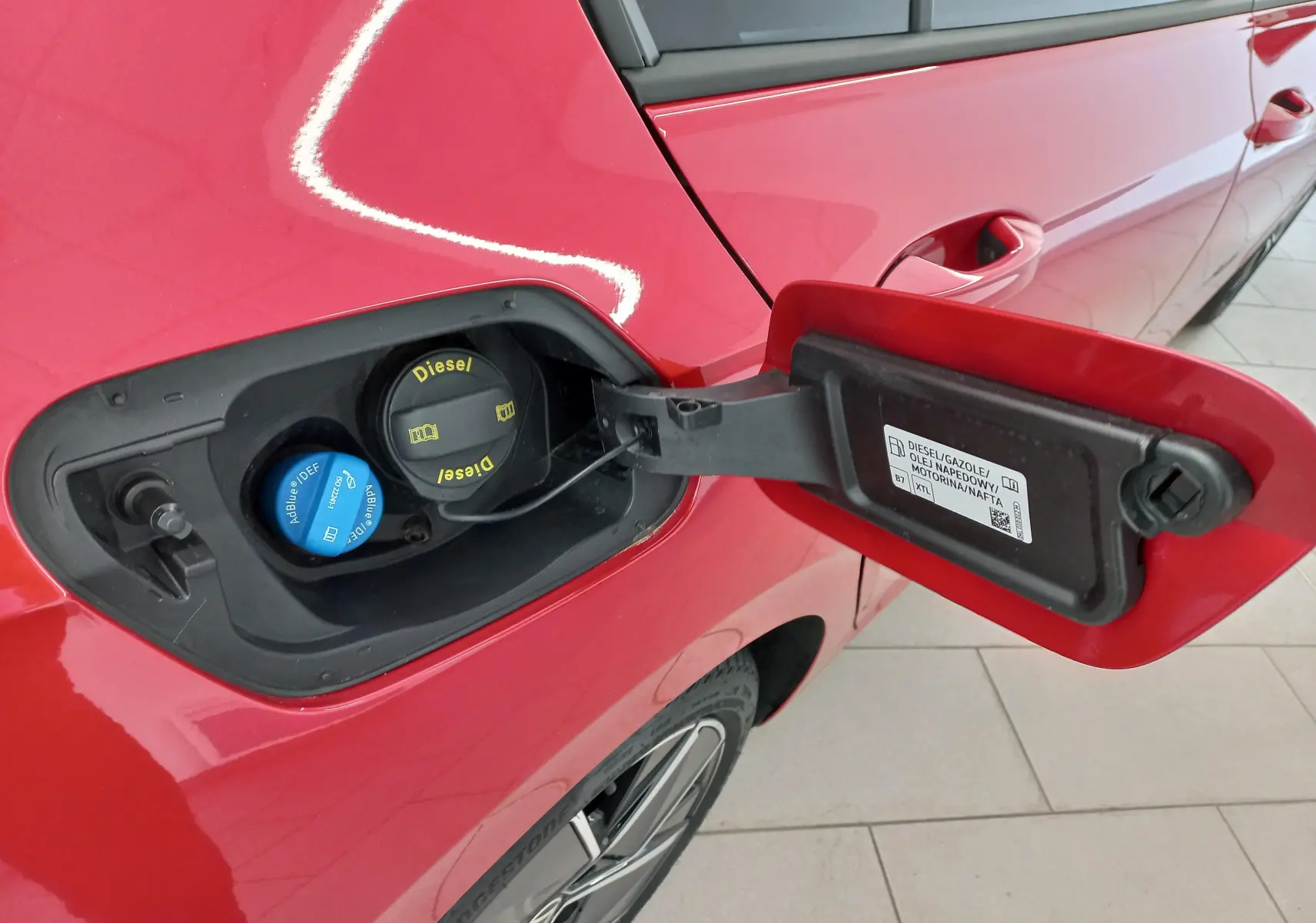 Vue rapprochée de la trappe à carburant ouverte côté gauche d'une Volkswagen Golf Rouge Roi avec bouchons Diesel et AdBlue visibles.