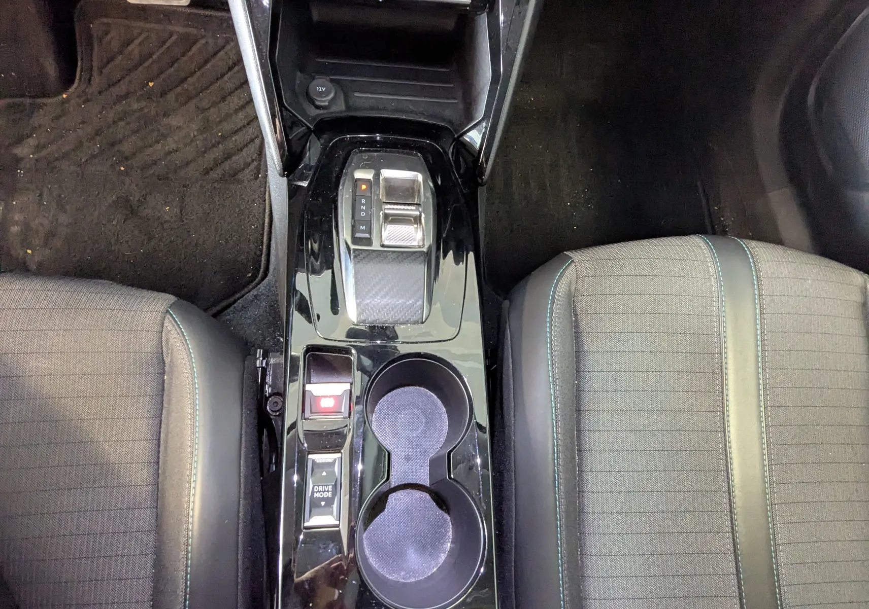 Vue plongeante sur la console centrale noire brillante du Peugeot 2008 1.5 BlueHDi, avec levier de vitesses et porte-gobelets.