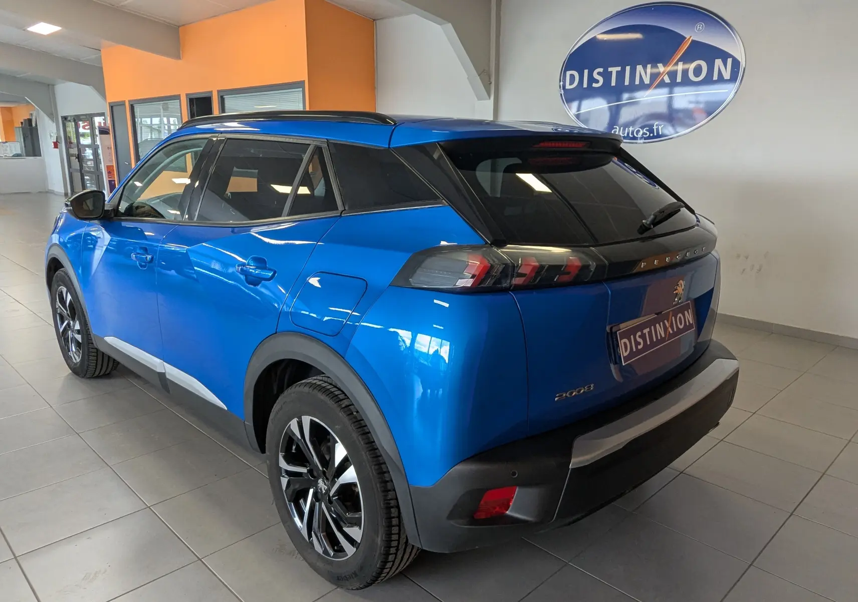Vue 3/4 arrière droit d'un Peugeot 2008 bleu métallisé avec toit noir dans un showroom intérieur.