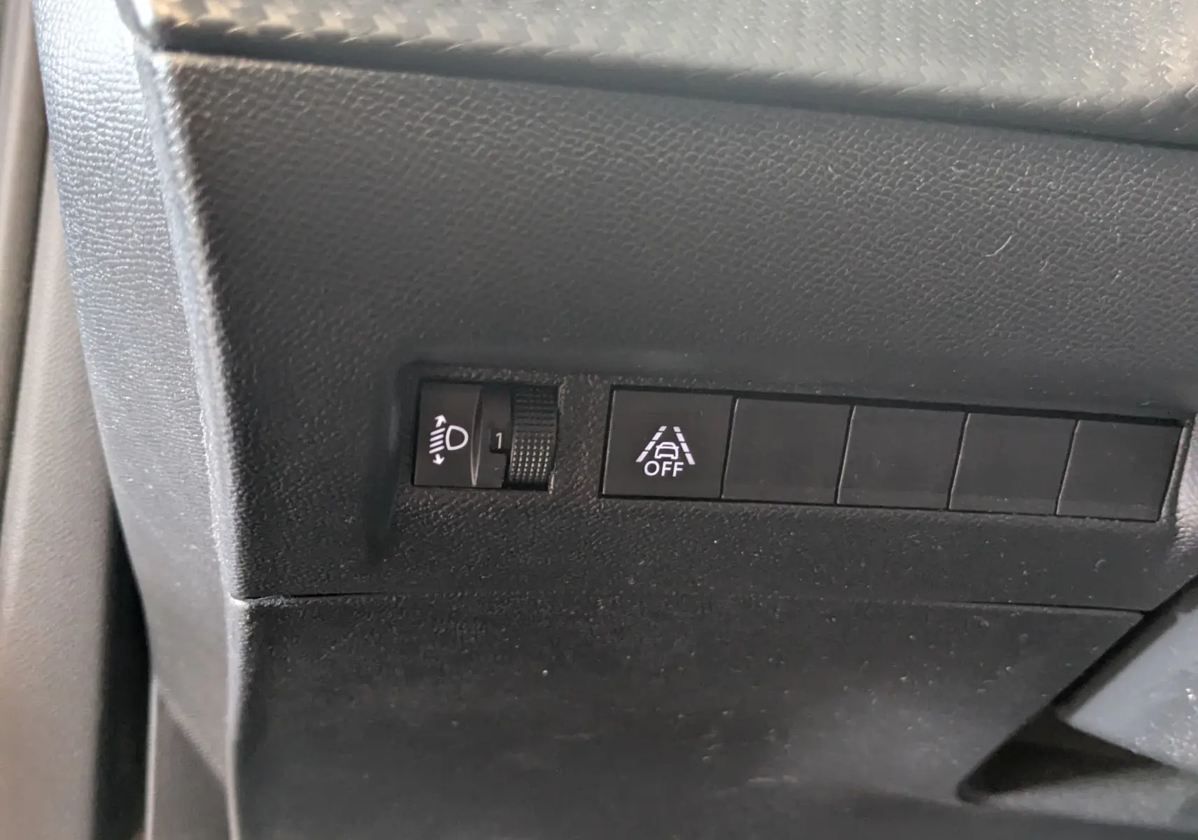 Gros plan sur les commandes de réglage des phares et d'activation de l'alerte de franchissement de ligne dans un Peugeot 2008 bleu.