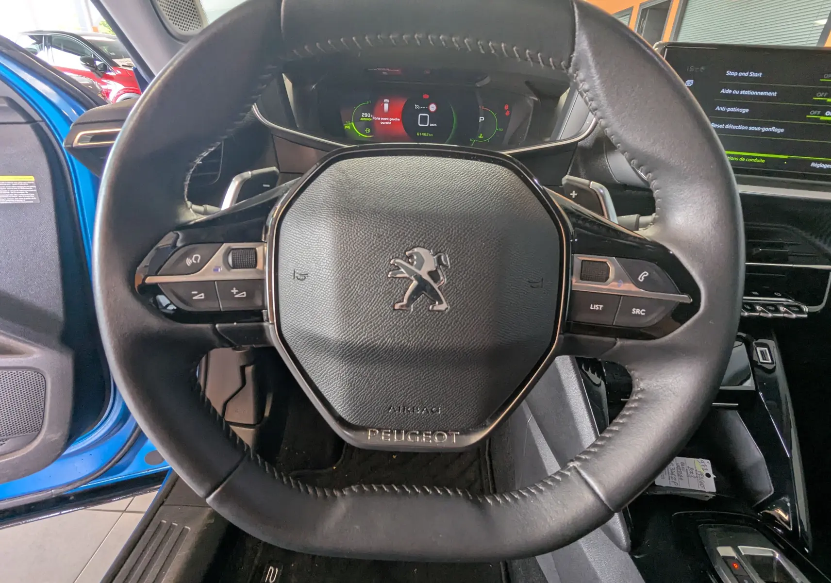Vue rapprochée du volant cuir noir de la Peugeot 2008 bleu 2022, avec tableau de bord numérique et écran tactile visible.