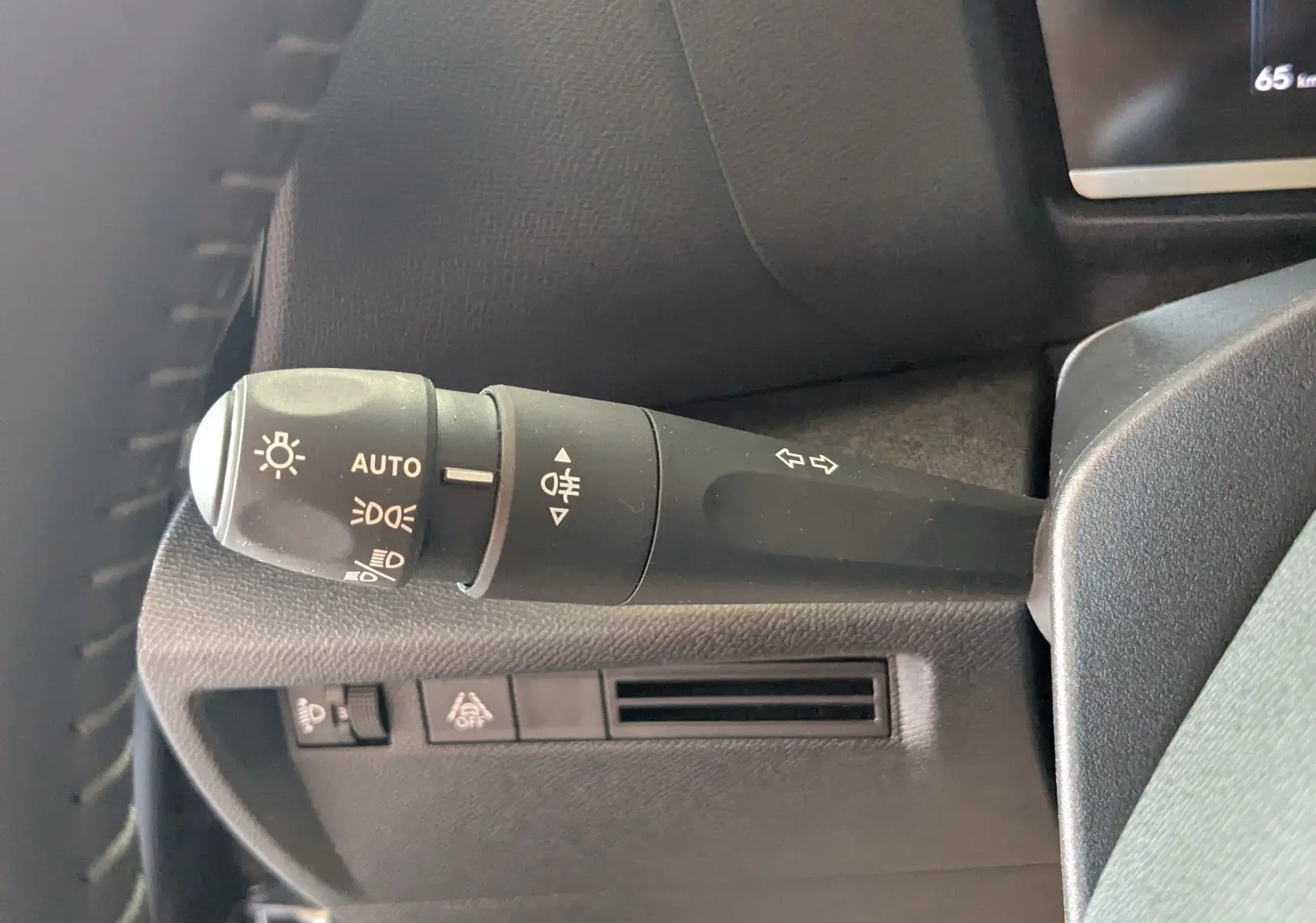 Gros plan sur la manette de commande des phares et clignotants à gauche du volant dans l'habitacle gris du Citroën C4 Hybrid 2025.