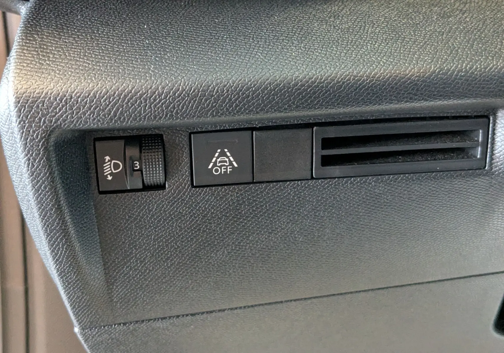 Vue rapprochée des commandes noires du tableau de bord du Citroën C4 Hybrid 145 gris Mercury, avec bouton de régulation des phares et désactivation de l'alerte de franchissement de ligne.
