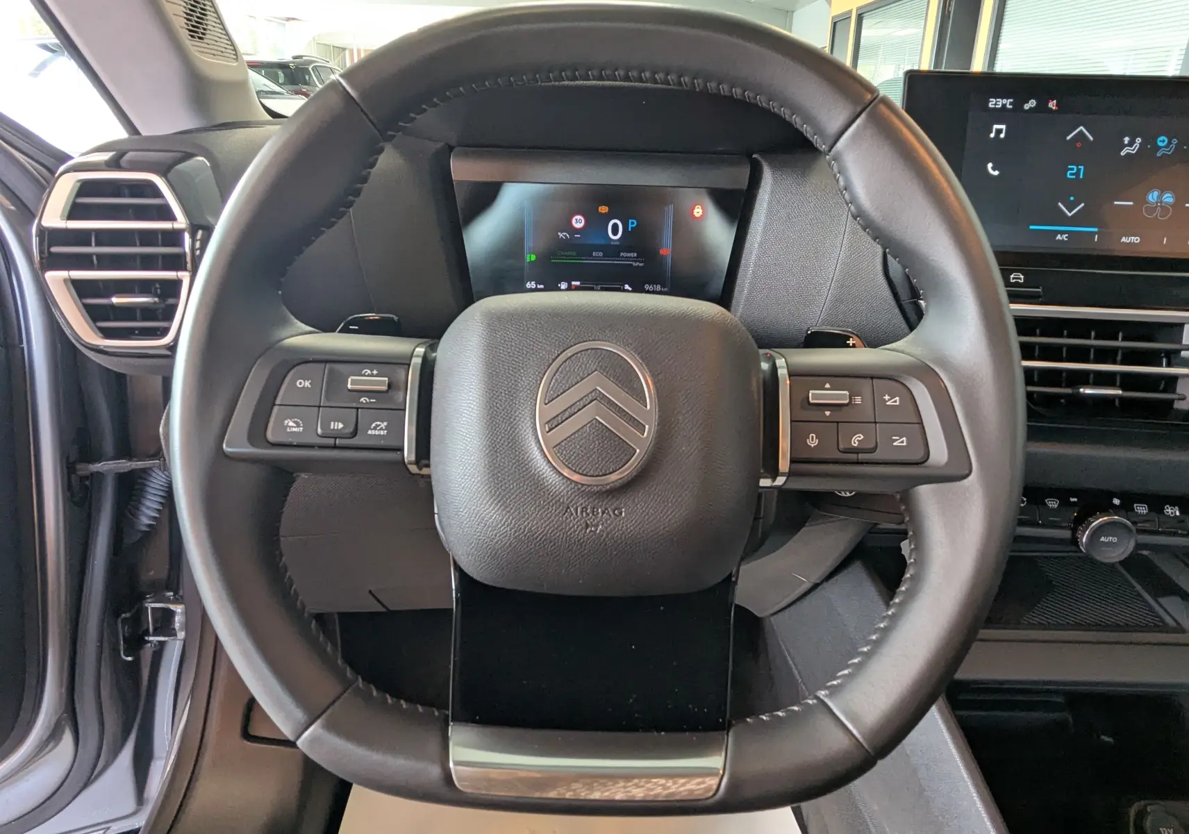 Vue rapprochée du volant noir de la Citroën C4 Hybrid 145 E-DCS6 Plus avec tableau de bord digital et commandes intégrées.