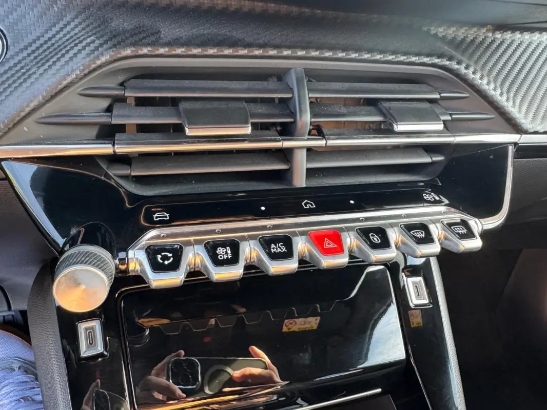 Gros plan sur la console centrale du Peugeot 2008 Hybrid noir, avec commandes climatisation et boutons chromés.