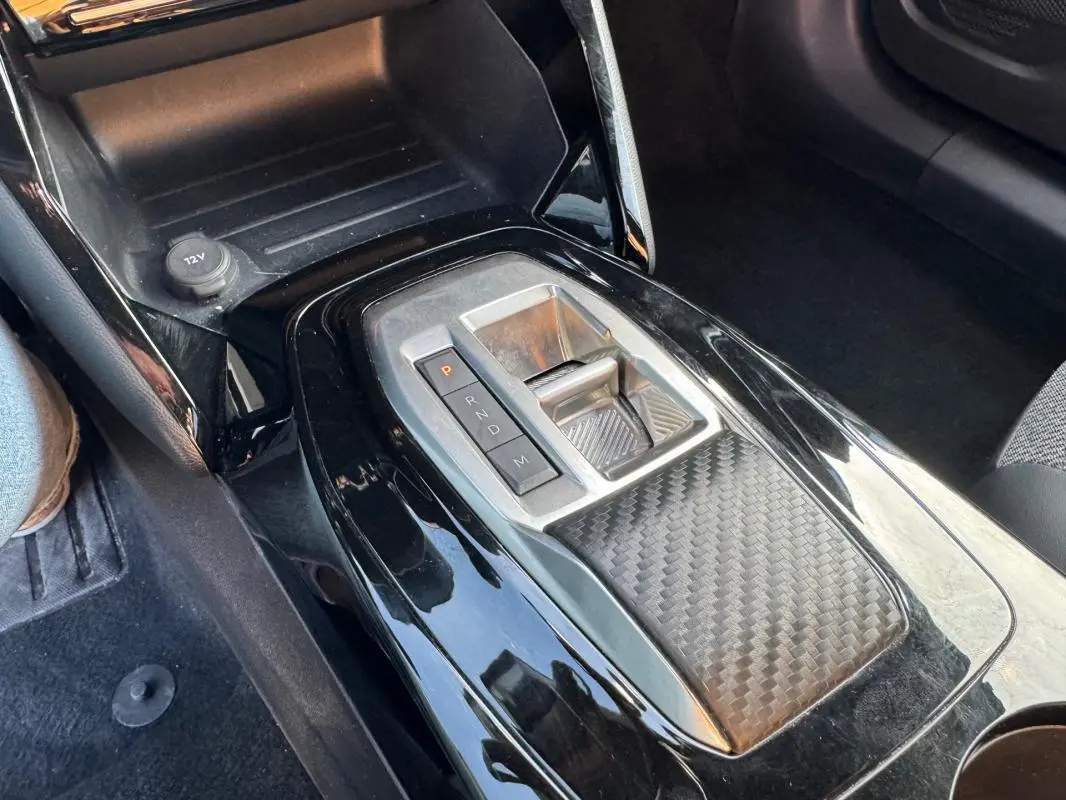 Gros plan sur la console centrale noire brillante du Peugeot 2008 Hybrid 136 e-DCS6 Allure avec levier de boîte auto.