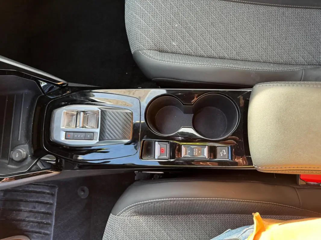 Vue plongeante sur la console centrale noire brillante du Peugeot 2008 Hybrid 136 avec commandes de boîte auto et porte-gobelets.