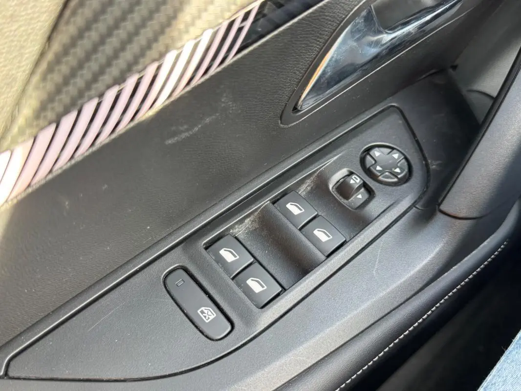 Gros plan sur les commandes des vitres électriques côté gauche d’une Peugeot 2008 Hybrid noire, avec réglage des rétroviseurs.