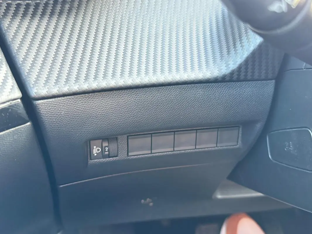 Détail intérieur côté gauche du tableau de bord noir avec commande de réglage des phares sur Peugeot 2008 Hybrid 136 e-DCS6 Allure.