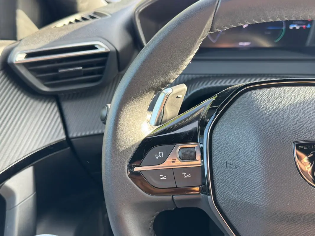 Gros plan sur le volant noir de la Peugeot 2008 Hybrid 136 e-DCS6 Allure avec commandes intégrées et tableau de bord partiel.