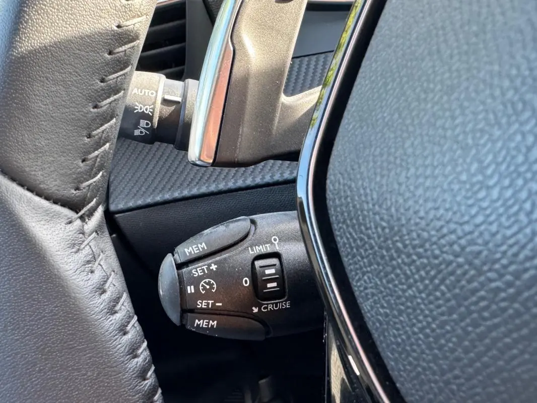 Gros plan sur la commande de régulateur de vitesse au volant cuir noir du Peugeot 2008 Hybrid 136 e-DCS6 Allure.