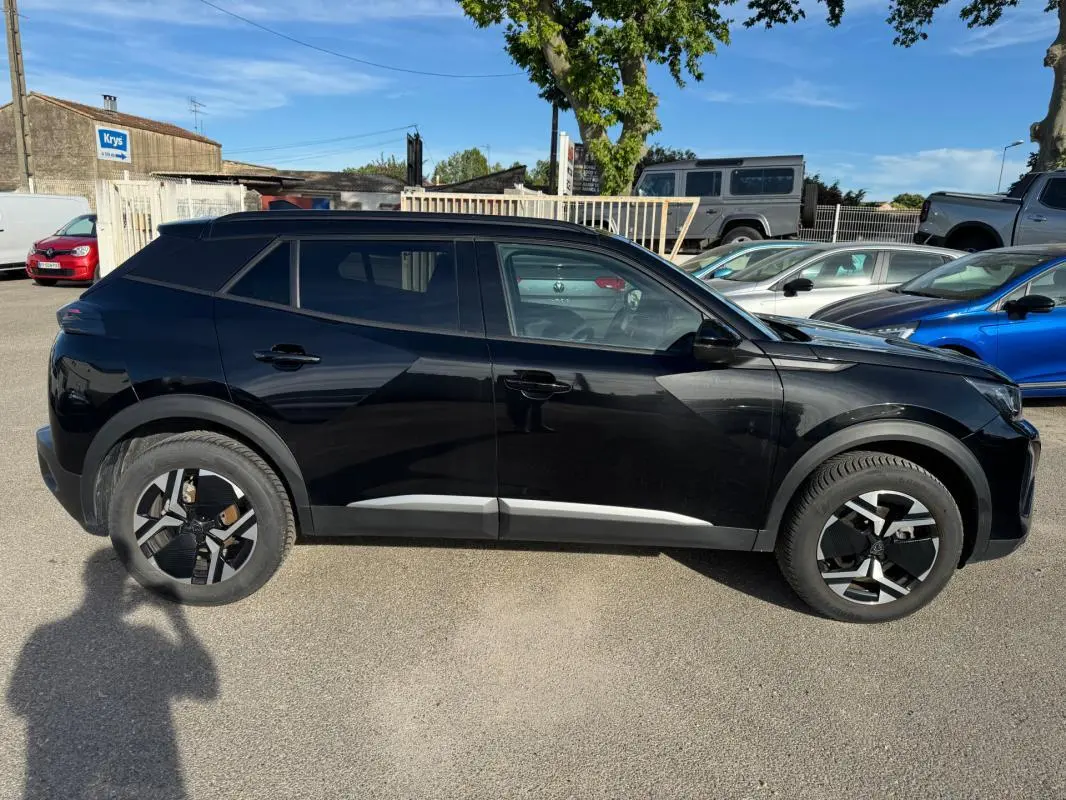 Profil côté gauche du Peugeot 2008 Hybrid 136 Allure noir avec jantes alliage 17 pouces et barres de toit visibles.