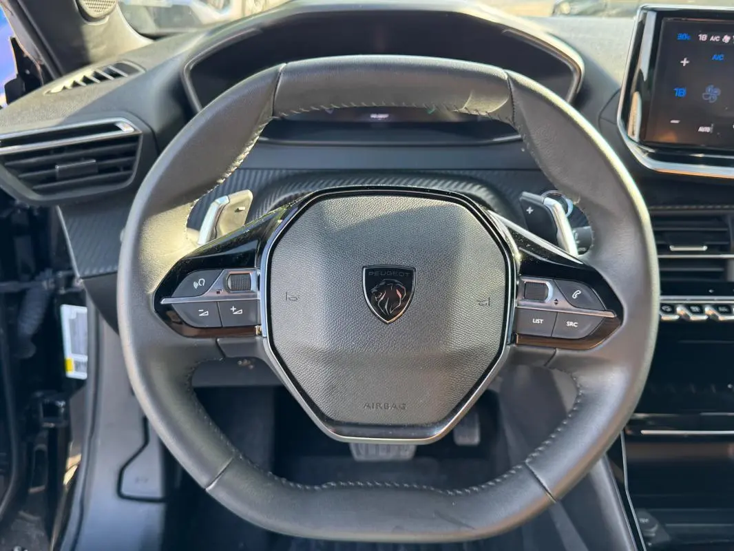 Vue rapprochée du volant noir de la Peugeot 2008 Hybrid 136 e-DCS6 Allure avec commandes intégrées et tableau de bord numérique.