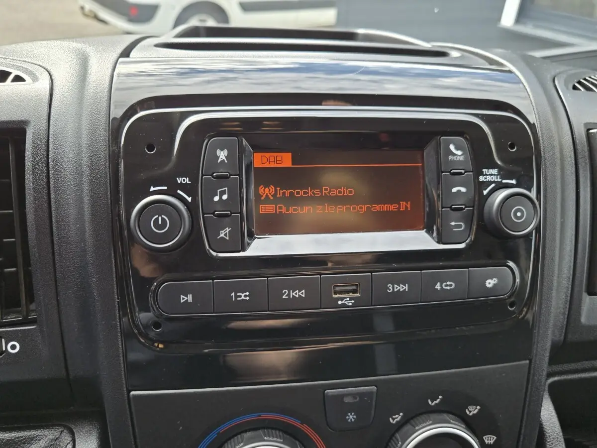 Gros plan sur la console centrale noire du tableau de bord du Fiat Ducato Fourgon avec écran radio et commandes audio.