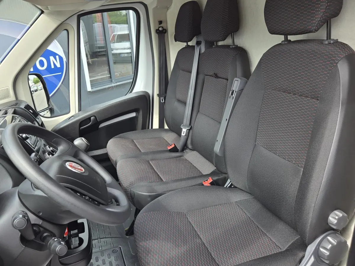 Vue intérieure côté conducteur du Fiat Ducato Fourgon 2023, montrant les sièges noirs avec motifs rouges et le volant.