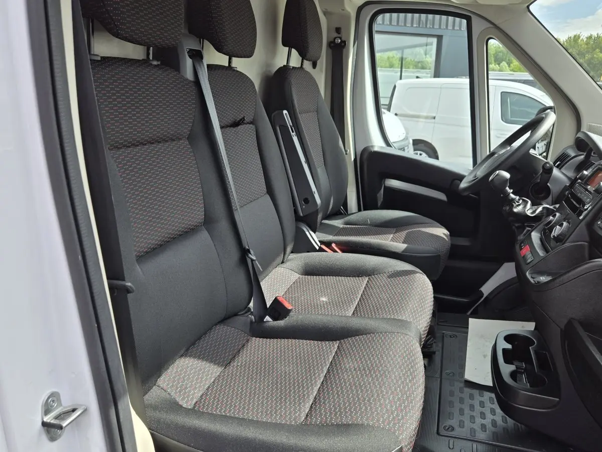 Vue intérieure côté conducteur du Fiat Ducato Fourgon blanc 2023, montrant les sièges avant en tissu noir à motifs rouges.