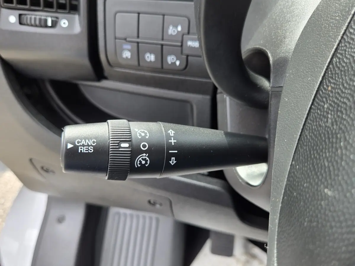 Gros plan sur la commande de régulateur de vitesse à gauche du volant dans l'habitacle noir du Fiat Ducato Fourgon blanc.
