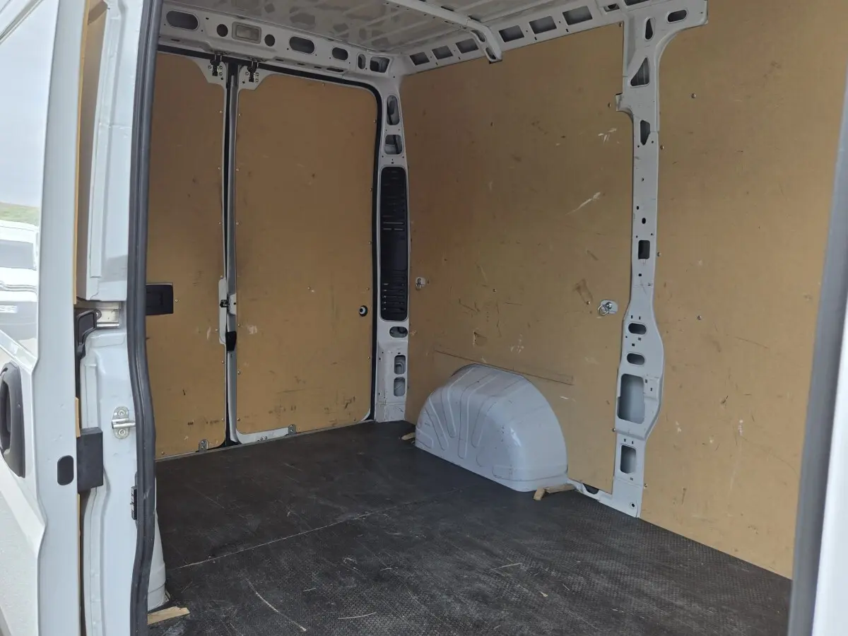 Vue intérieure arrière du fourgon blanc Fiat Ducato MH2 2023, montrant l'espace de chargement avec cloison pleine en bois.