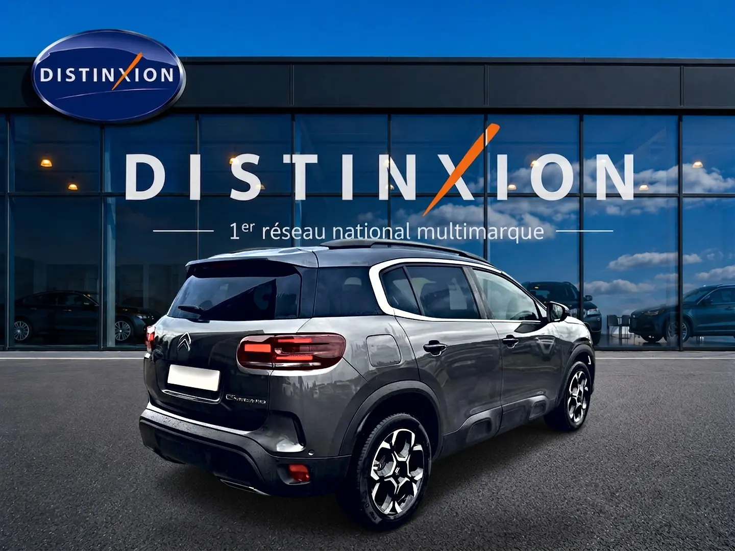 Vue 3/4 arrière droite du Citroën C5 Aircross gris platinium avec jantes alu, stationné devant une vitrine Distinxion.