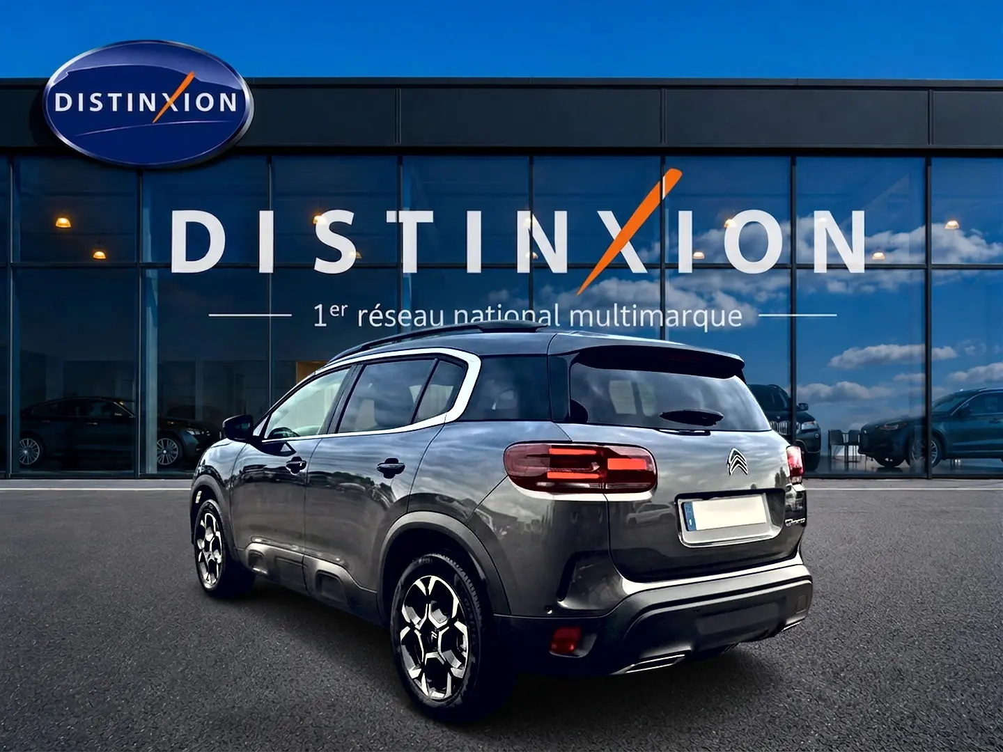 Vue 3/4 arrière droite du Citroën C5 Aircross gris platinium avec jantes alu et barres de toit visibles.