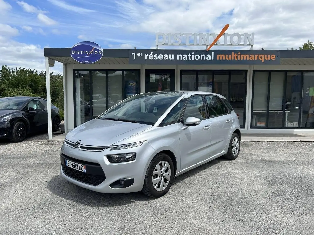 Citroën C4 Picasso gris aluminum vue 3/4 avant droit, stationnée devant un showroom Distinxion.