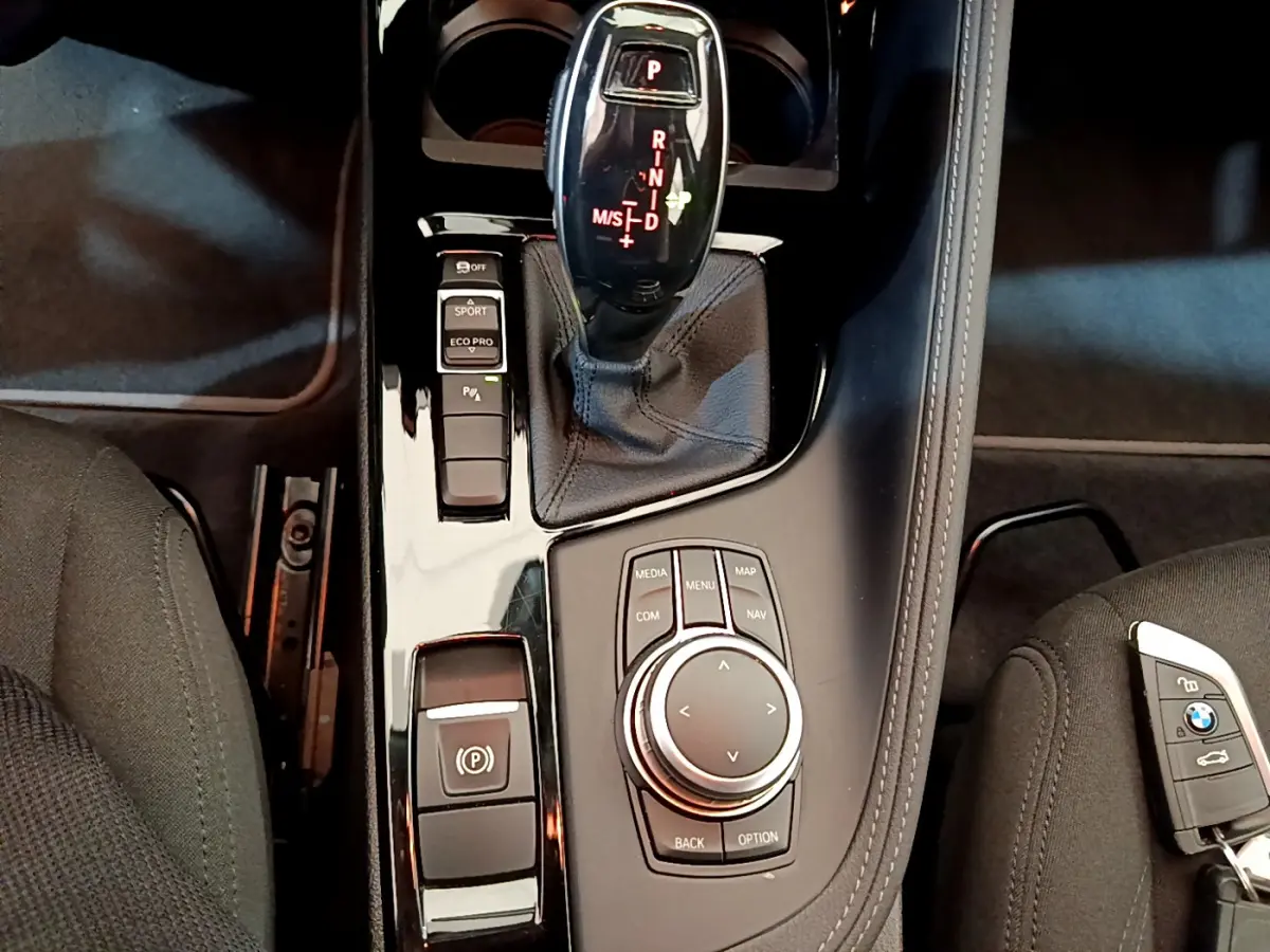 Gros plan sur la console centrale noire du BMW X2 blanc 2023, avec levier de vitesses automatique et molette de contrôle multimédia.