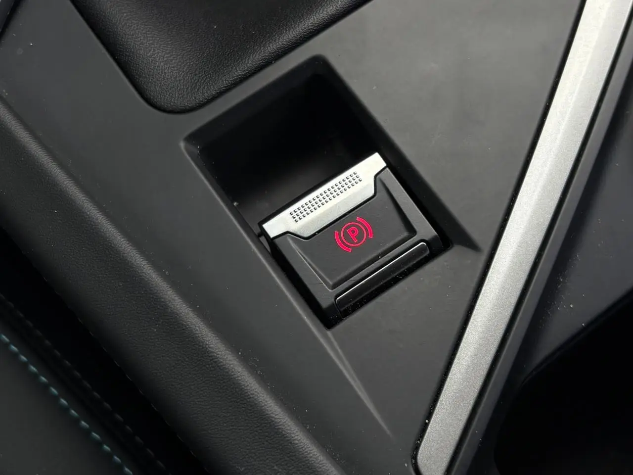 Gros plan sur le bouton de frein de parking électrique rouge dans l'accoudoir central de la Peugeot 308 Bleu Obsession 2024.
