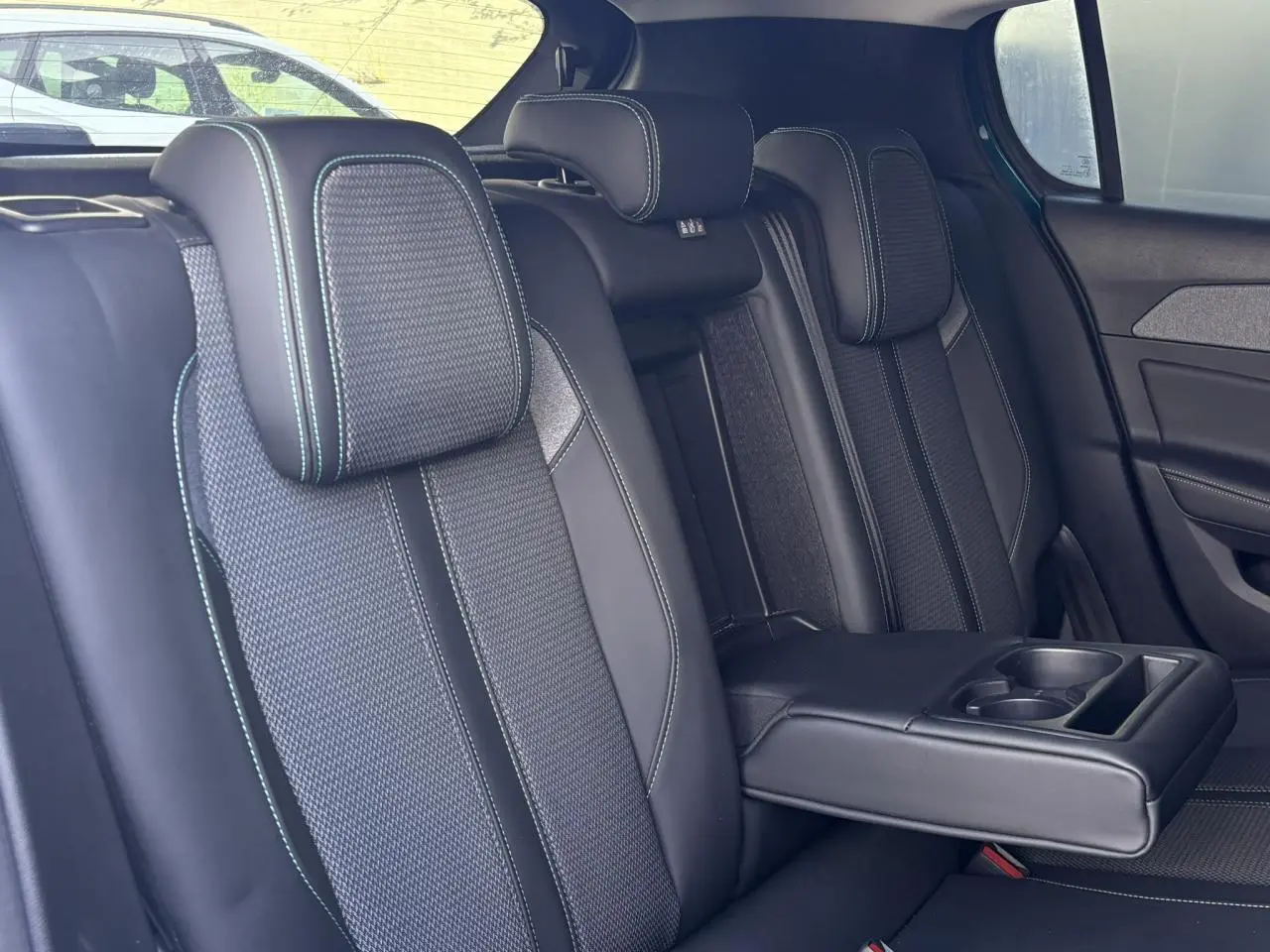 Vue intérieure des sièges arrière de la Peugeot 308 2024, sellerie tri matières noire avec surpiqûres bleues et accoudoir central déplié.