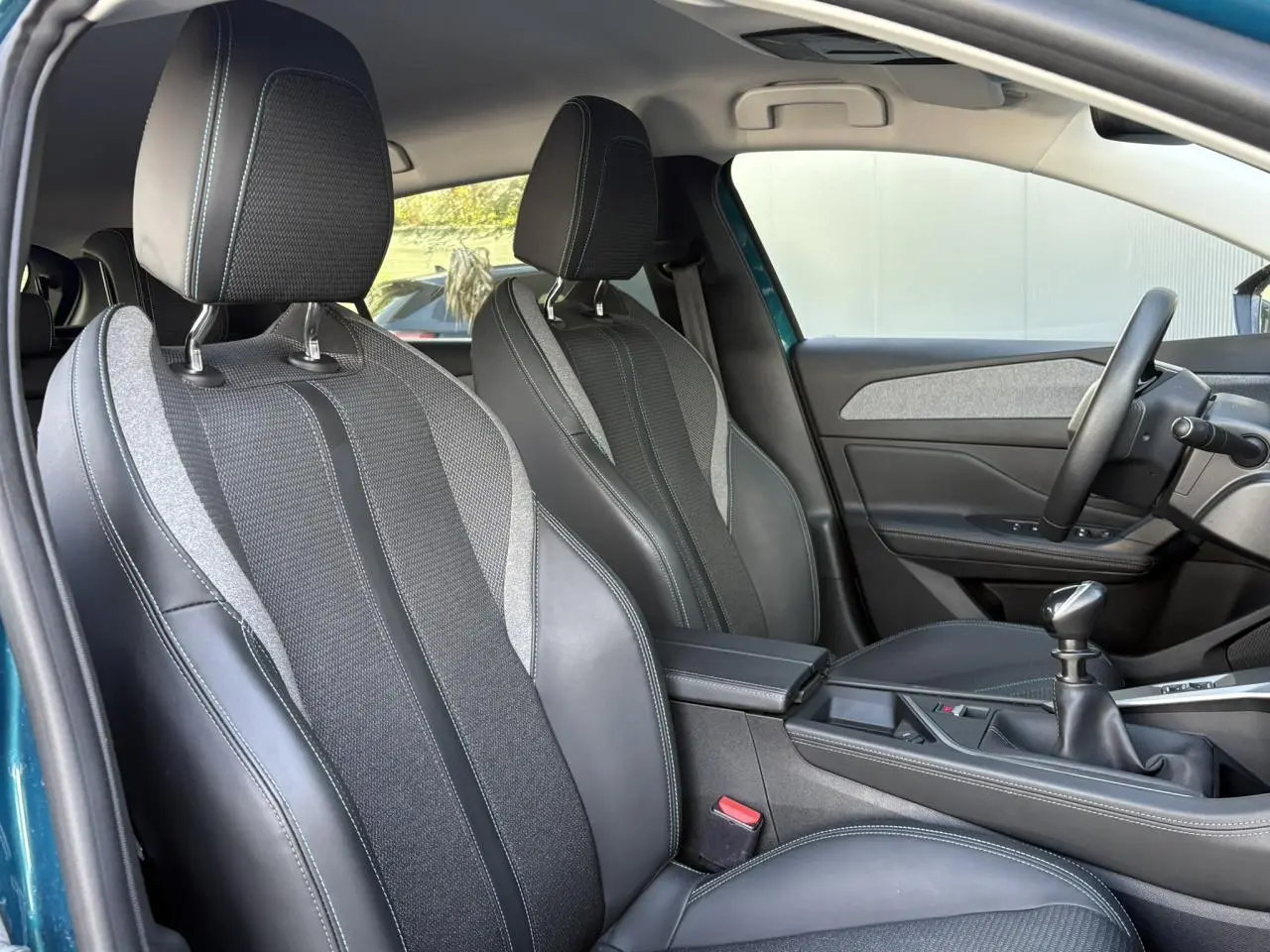 Vue intérieure côté conducteur de la Peugeot 308 Bleu Obsession, montrant sièges TEP/tissu et levier de vitesses manuel.