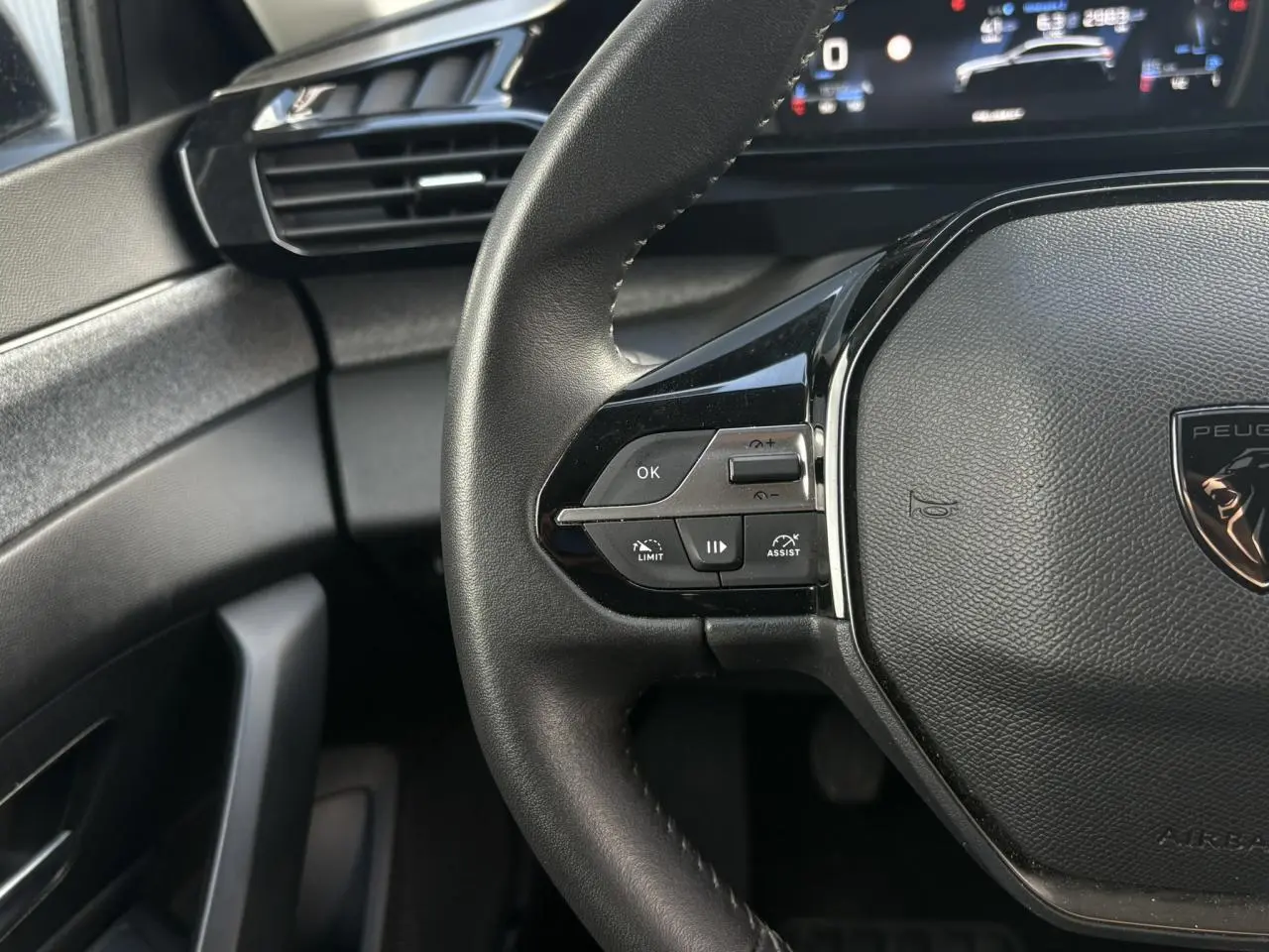 Gros plan sur le volant cuir noir de la Peugeot 308 2024 avec commandes intégrées côté gauche et tableau de bord numérique.