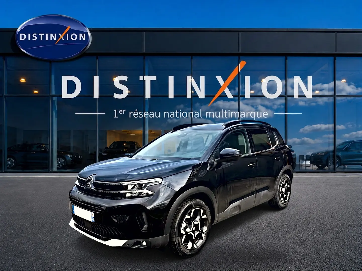 Citroën C5 Aircross noir vue 3/4 avant droit, avec jantes alu et barres de toit visibles devant showroom Distinxion.