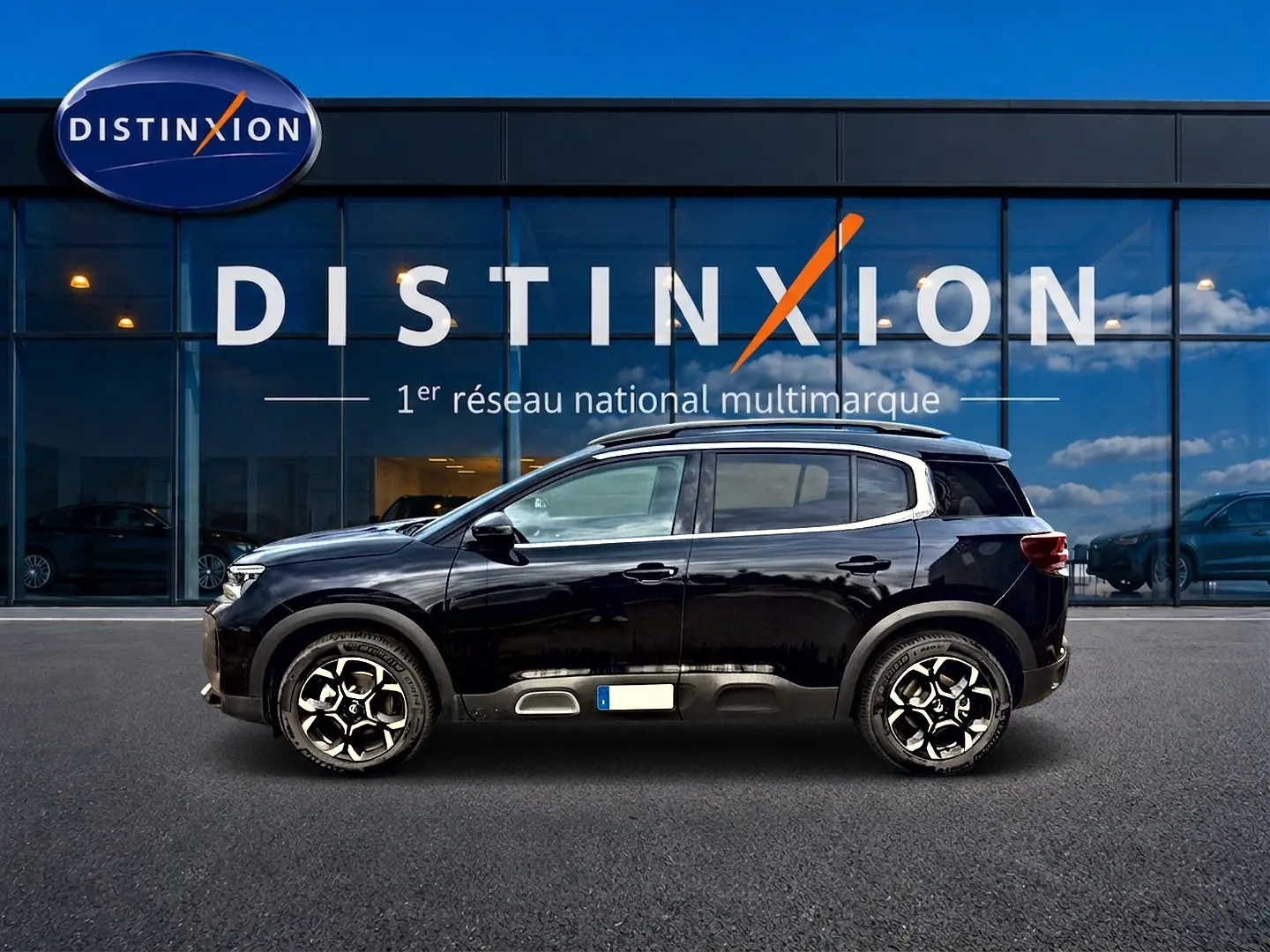 Profil côté gauche d'un Citroën C5 Aircross noir 2025 avec jantes alu et barres de toit devant une vitrine Distinxion.