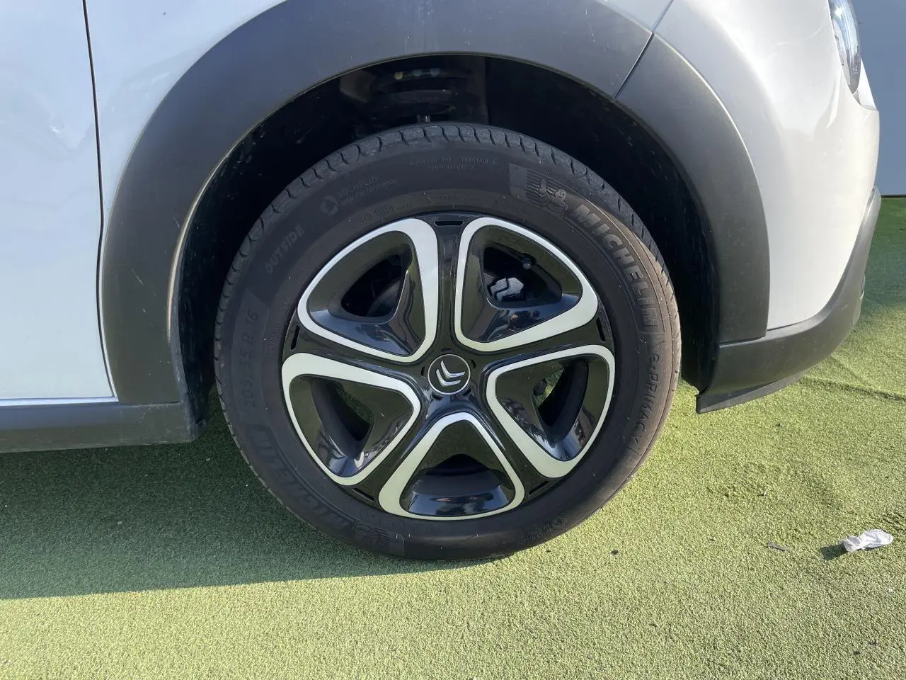 Gros plan sur la roue avant gauche d'une Citroën C3 blanche avec enjoliveur 3D noir et chrome satin.