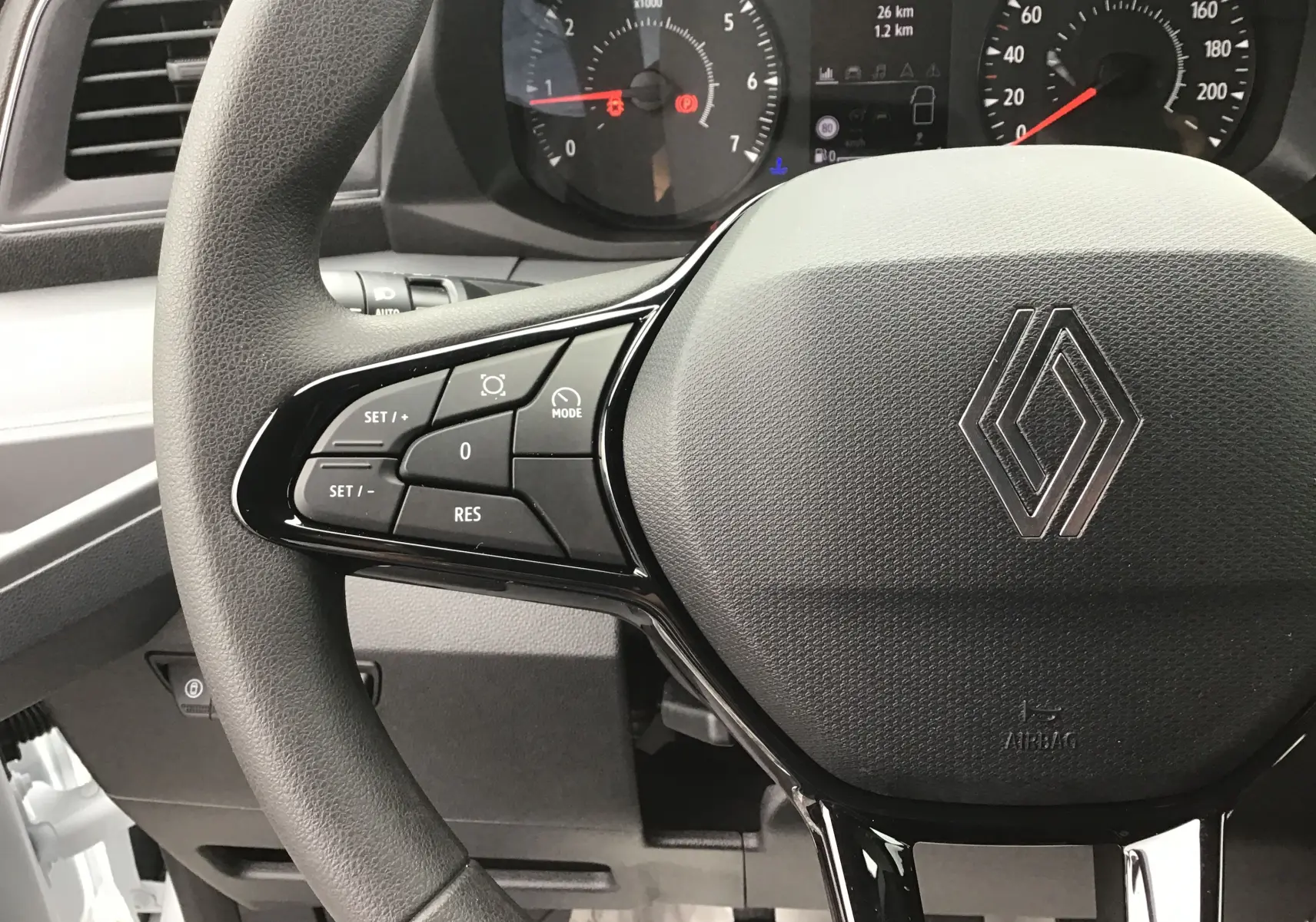 Gros plan sur le volant noir du Renault Master blanc 2025, avec commandes multifonctions à gauche et tableau de bord en arrière-plan.