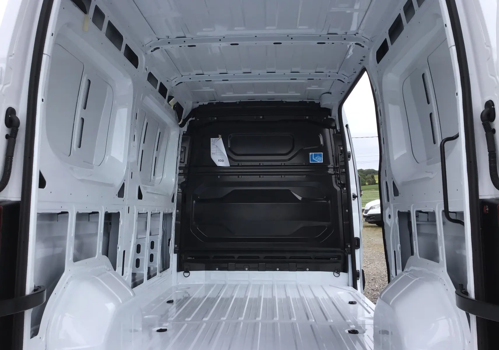 Intérieur vide du Renault Master blanc vu de l'arrière, montrant la cloison noire et la structure métallique du fourgon.