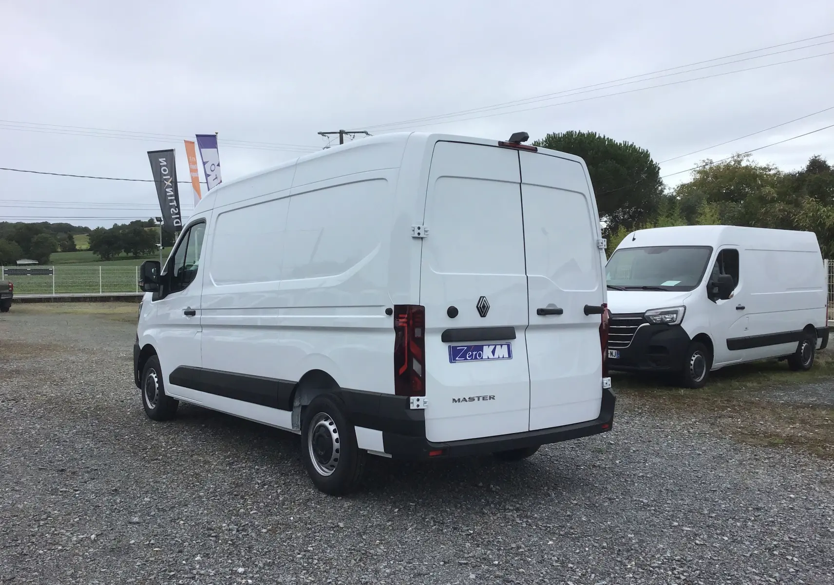 Vue 3/4 arrière droite d'un Renault Master blanc 2025 avec portes arrière fermées sur un parking extérieur.