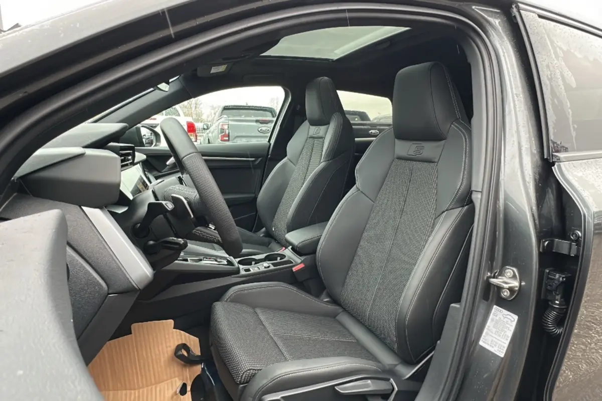 Vue intérieure côté conducteur de l'Audi A3 gris Daytona, sièges sport cuir-tissu avec logo S et toit panoramique.