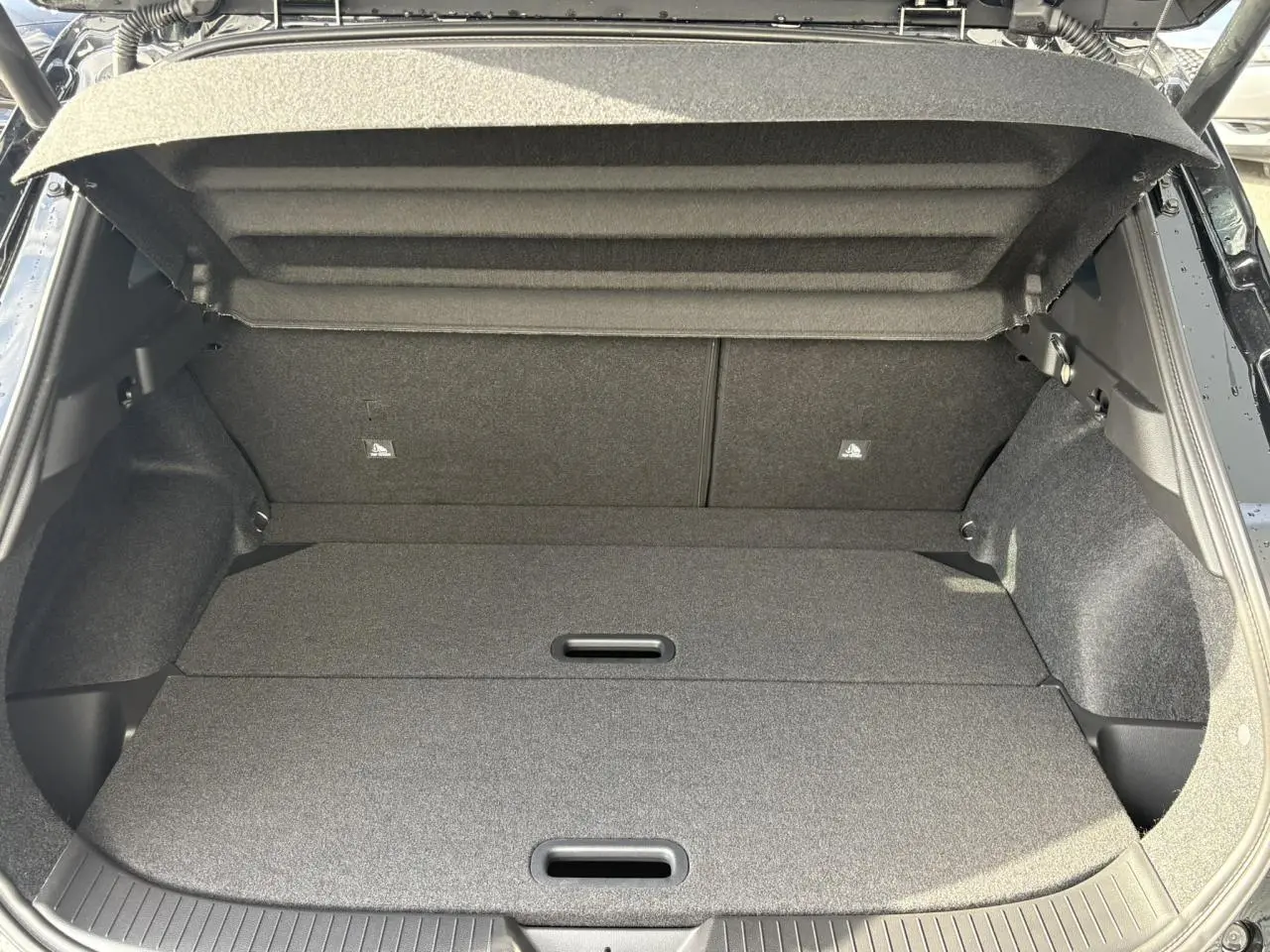 Coffre ouvert vu de l'arrière du Nissan Qashqai III noir, montrant un plancher de coffre modulable et tapis gris.