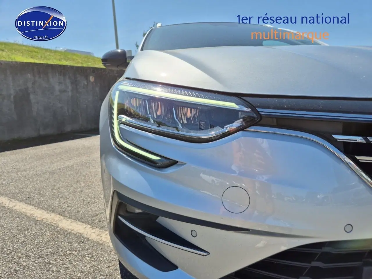 Gros plan sur le phare avant gauche d’une Renault Mégane Break gris Titanium avec détails LED et capteurs de stationnement.