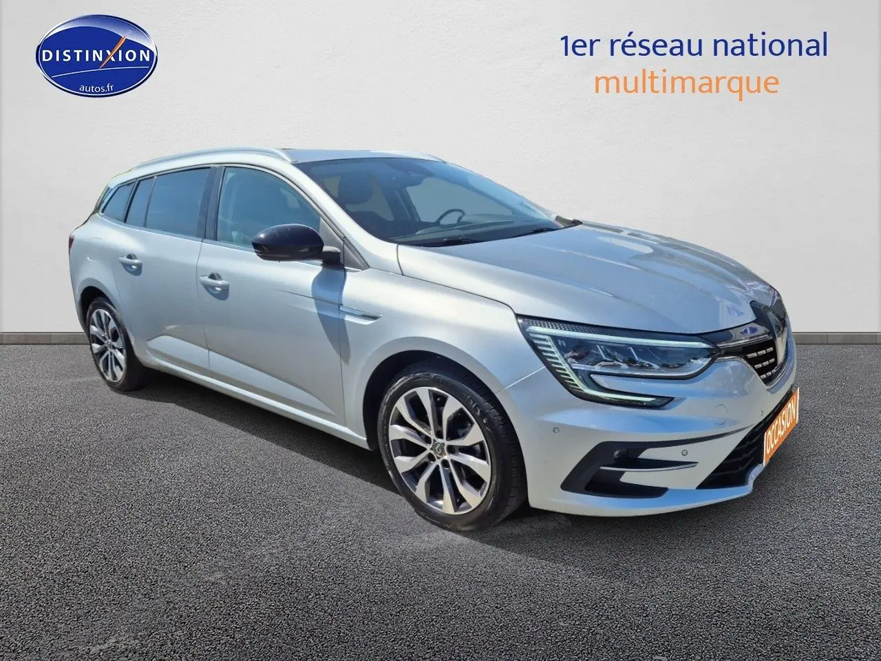 Renault Mégane Break gris titanium vue 3/4 avant droit, avec jantes alliage et barres de toit visibles.