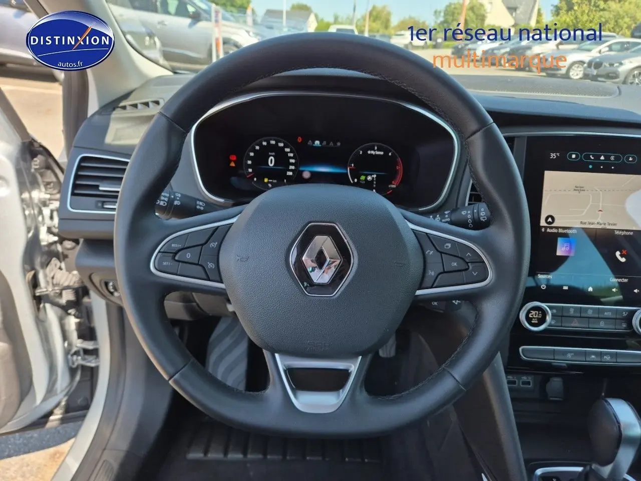Vue intérieure centrée sur le volant multifonction noir d'une Renault Mégane Break 2024 avec tableau de bord digital et écran tactile.
