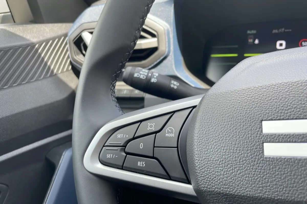 Gros plan sur le volant du Dacia Bigster 2025, montrant les commandes de régulateur et l'air vent hexagonal côté gauche.